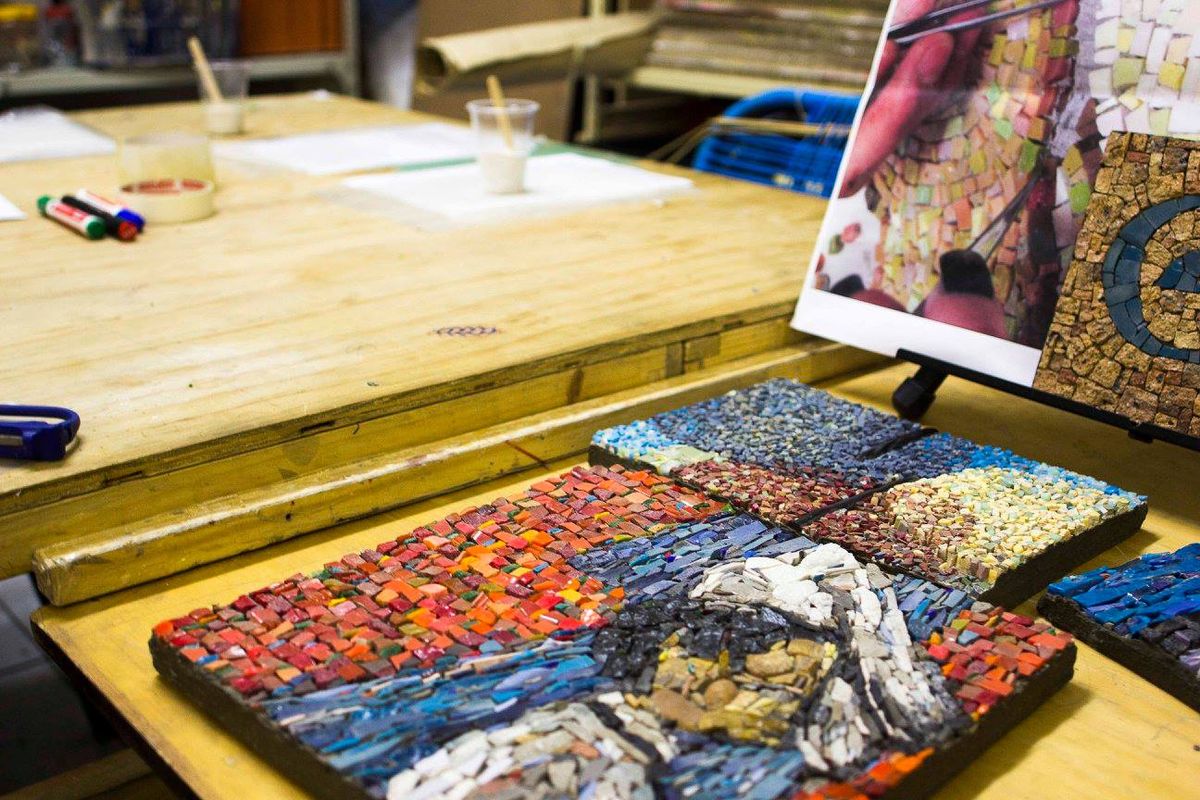 Four finished mosaic panels in blue, red and neutral tones laid out on a workbench