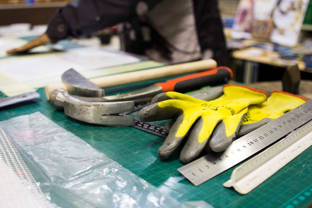 Hammers, a ruler and work gloves laid out on a studio cutting mat