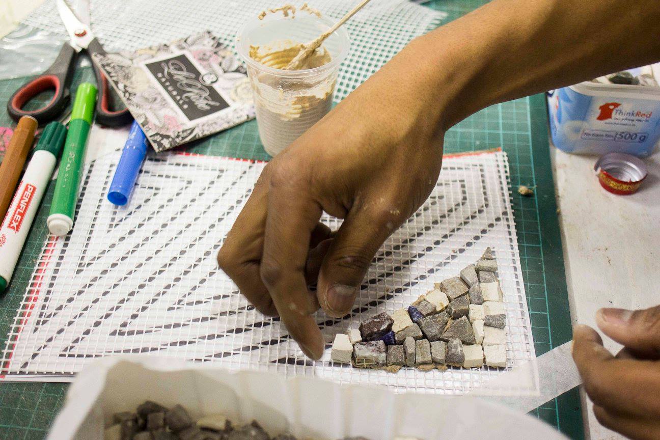 A close-up of a hand placing cut tile pieces onto mesh backing to build a mosaic