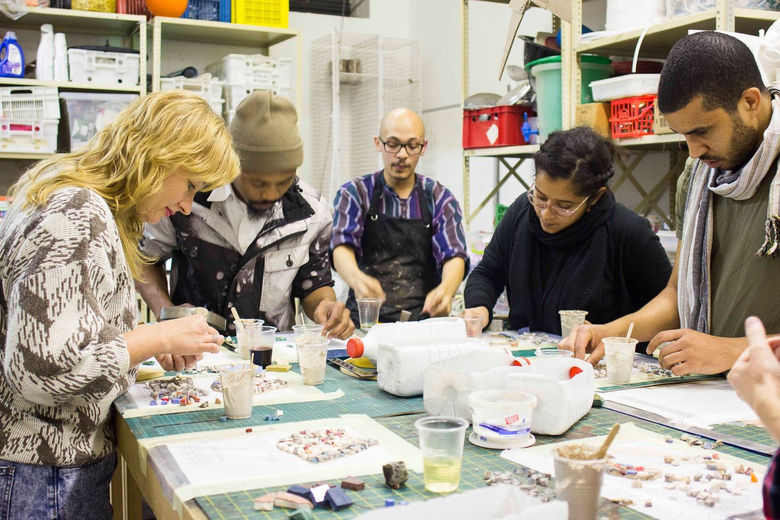 Five workshop participants gathered closely around a table, mosaic materials in front of them